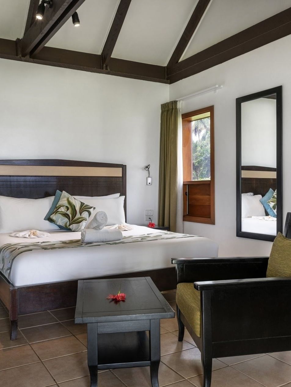 Wooden bed by a black armchair and coffee table with beams in Ocean View Villa at Tambua Sands Beach Resort