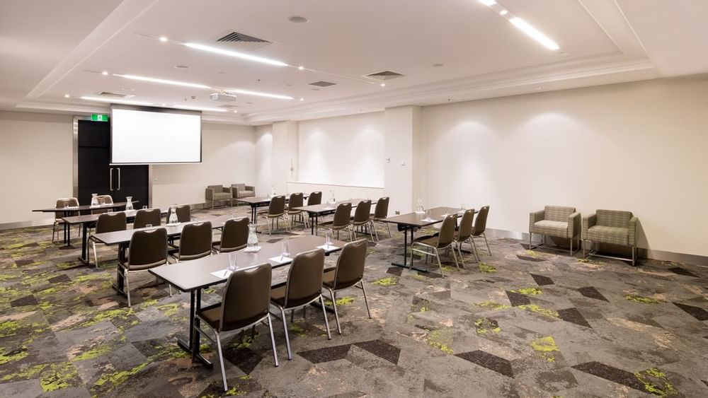 Protea with a classroom-style table setup facing a projector screen at Novotel Sydney International Airport