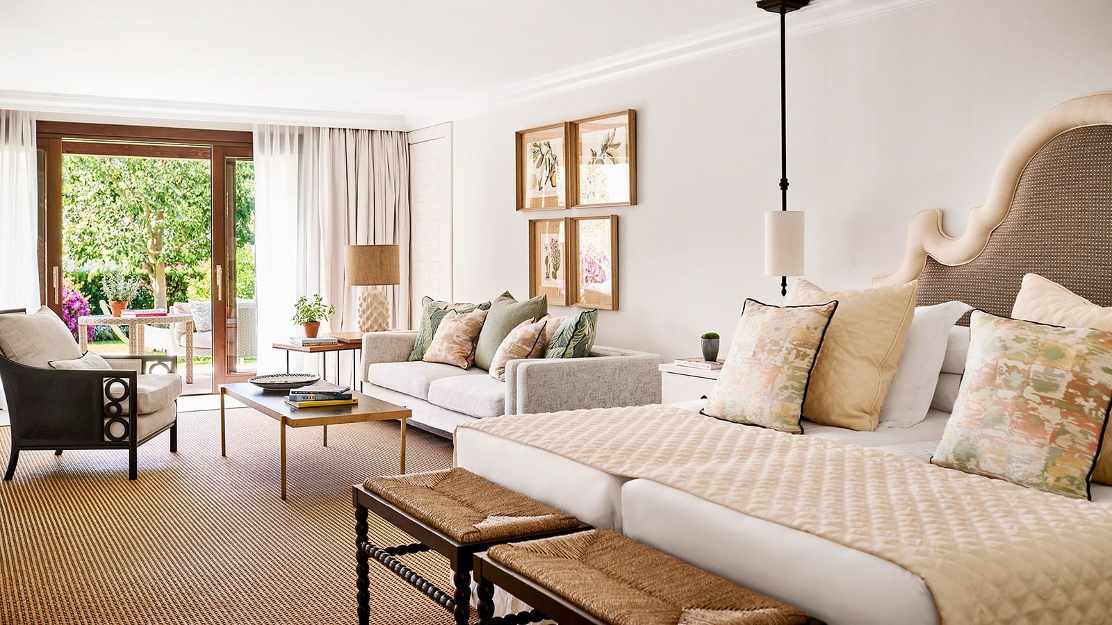 Junior Suite Deluxe with a bed, a sitting area, a woven rug, botanical artwork, & doors to a patio at Marbella Club