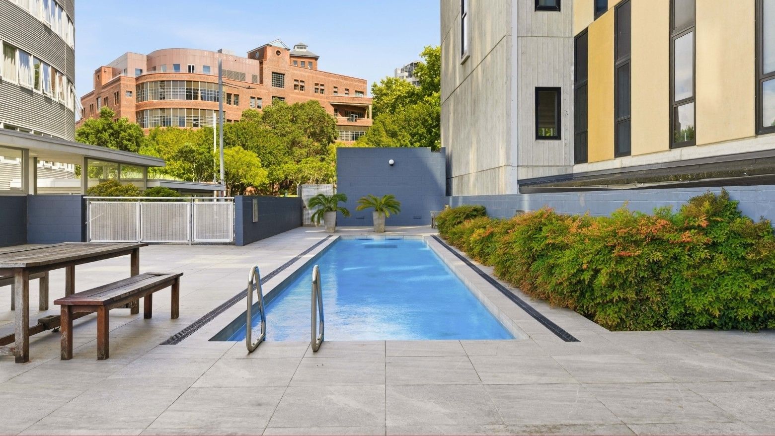 An outdoor swimming pool with wooden benches and table at Student Living Auckland Anzac.