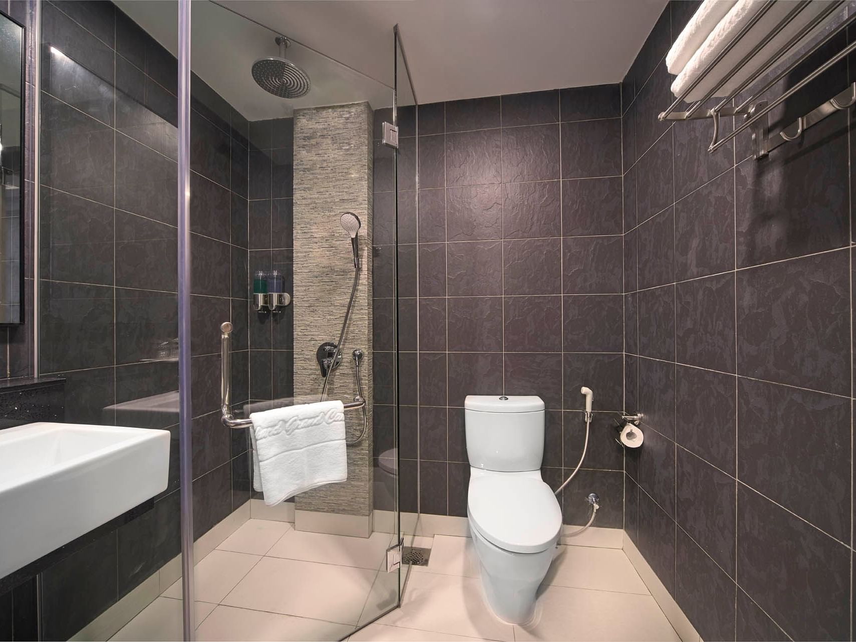 Image 11: Modern Studio Queen bathroom with glass shower, sleek toilet, dark tiled walls, and white sink at Orchard Grand Court