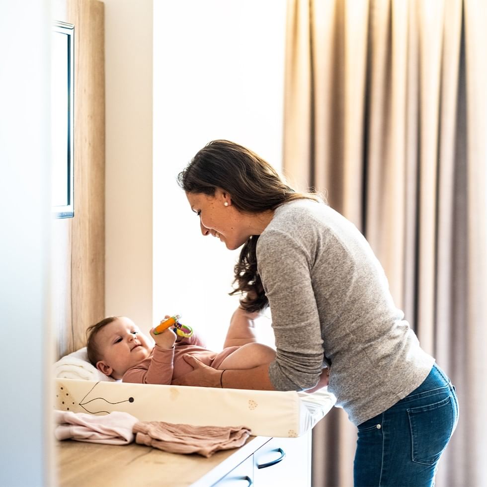 A woman leans over a baby on a changing table, smiling, as the baby holds a toy.