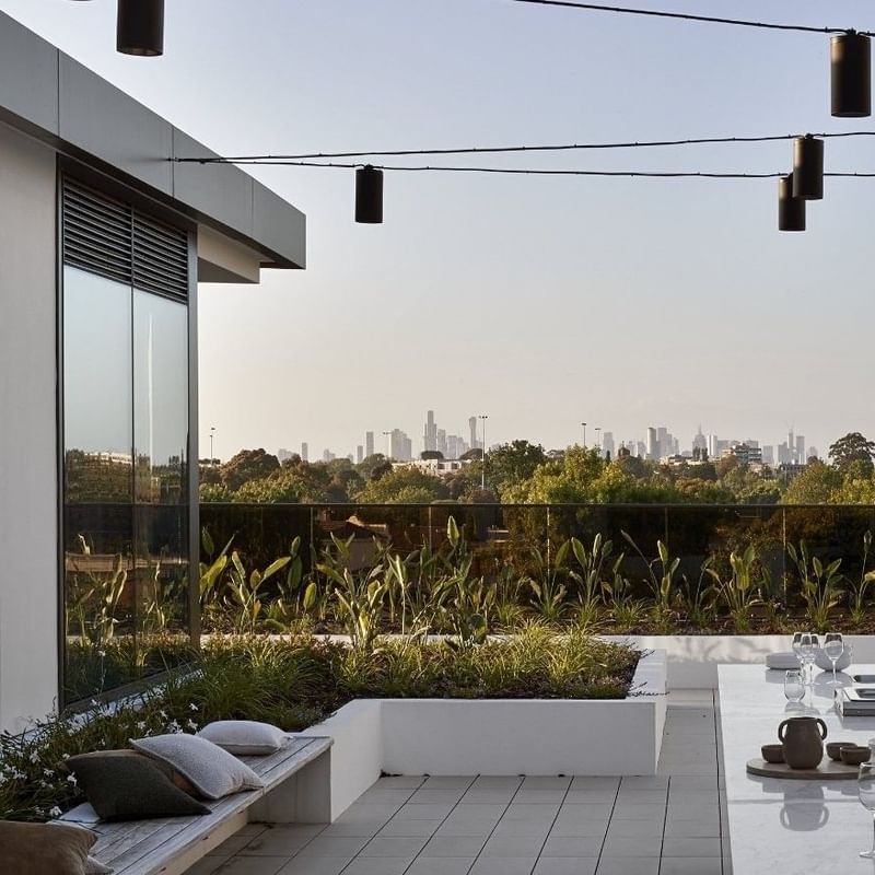 Outdoor kitchen with glass wall, hanging lights, bench, and skyline view.