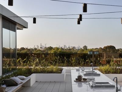Outdoor kitchen with glass wall, hanging lights, bench, and skyline view.