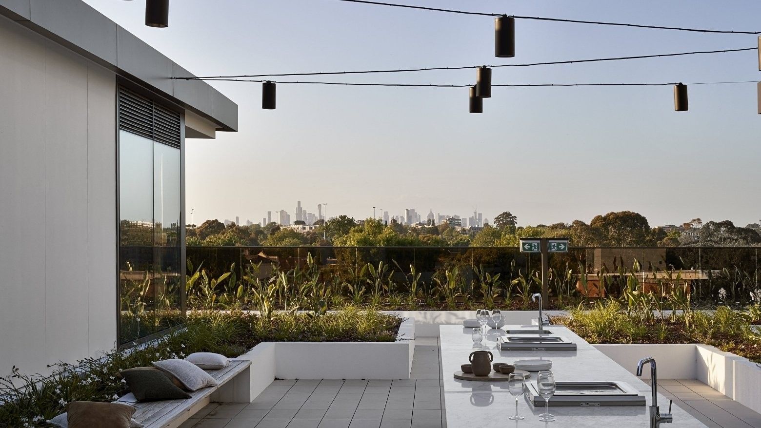 Outdoor kitchen with glass wall, hanging lights, bench, and skyline view.
