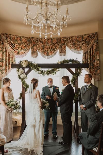 Wedding ceremony by a wooden flower arch held indoors at Pendray Inn & Tea House