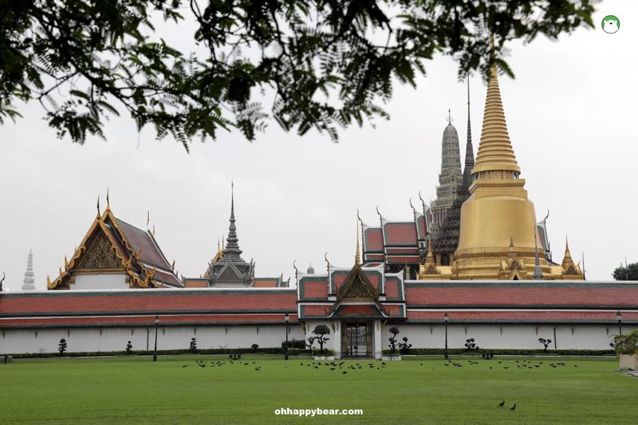 Golden spire of Wat Phra Kaew shines amid intricate rooftops, greenery in Bangkok's Grand Palace near The Okura Prestige Bangkok