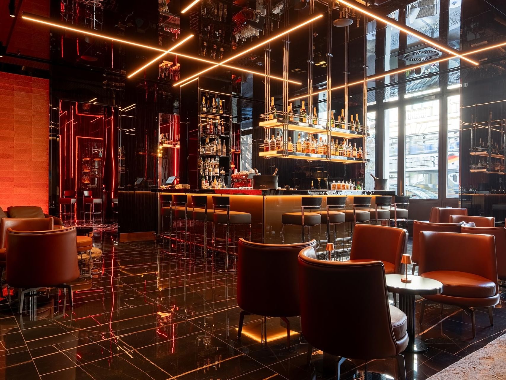 Modern hotel bar with orange leather seating, illuminated shelving, and reflective black floors at Titanic Gendarmenmarkt Berlin