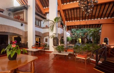 An open-air lobby with red tile floors, wooden furniture, and potted plants under a wooden and brick ceiling.