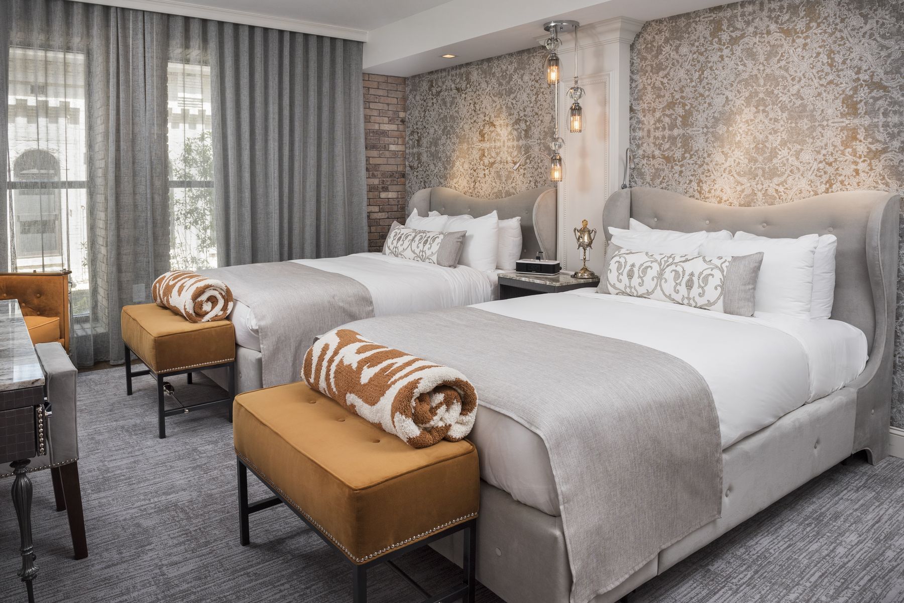 A hotel room with two beds, two benches, a lamp, and a window.