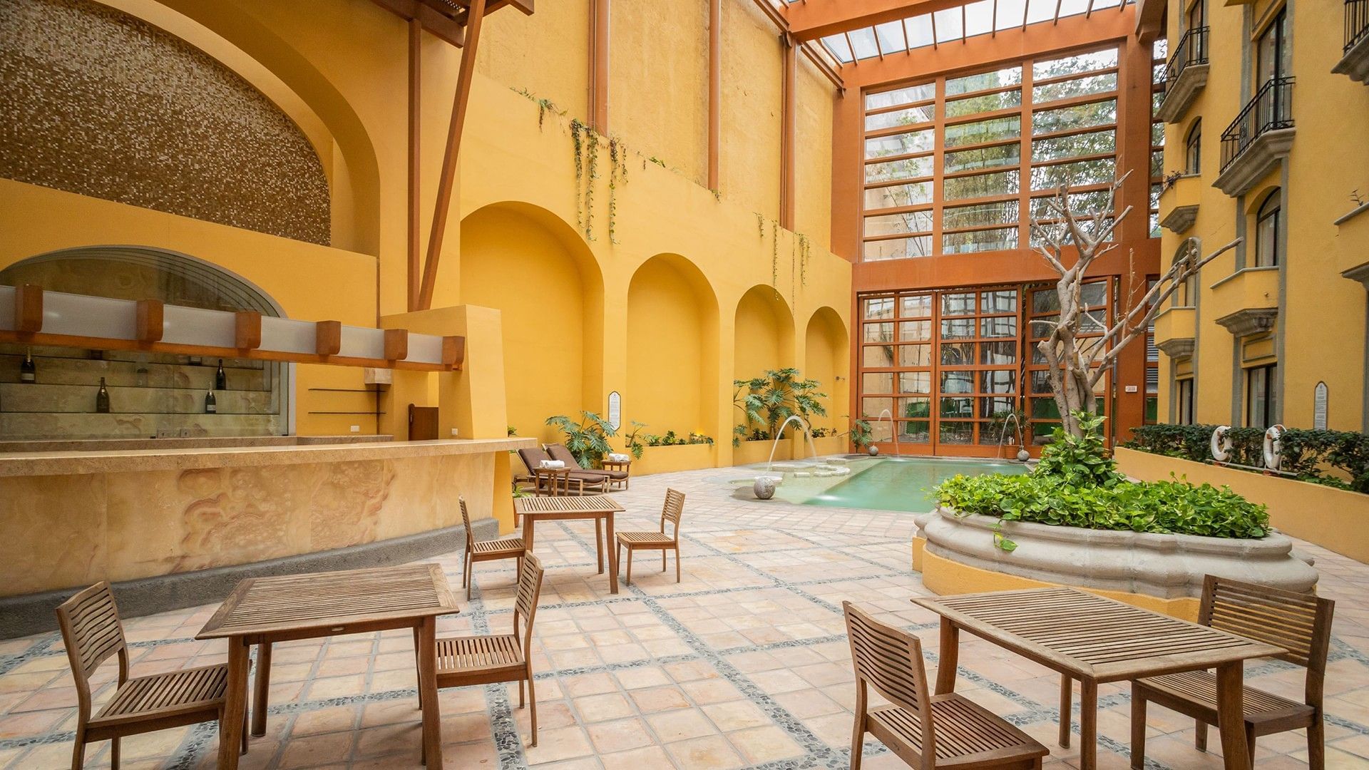 Beautiful sunlit courtyard with an outdoor pool, stone bar, and seating areas at Quinta Real Monterrey