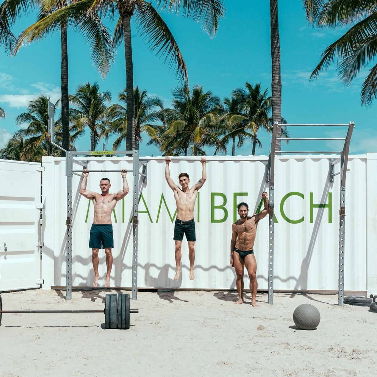 Three men perform fitness exercises on Miami Beach, with palm trees in the background near The Gaythering