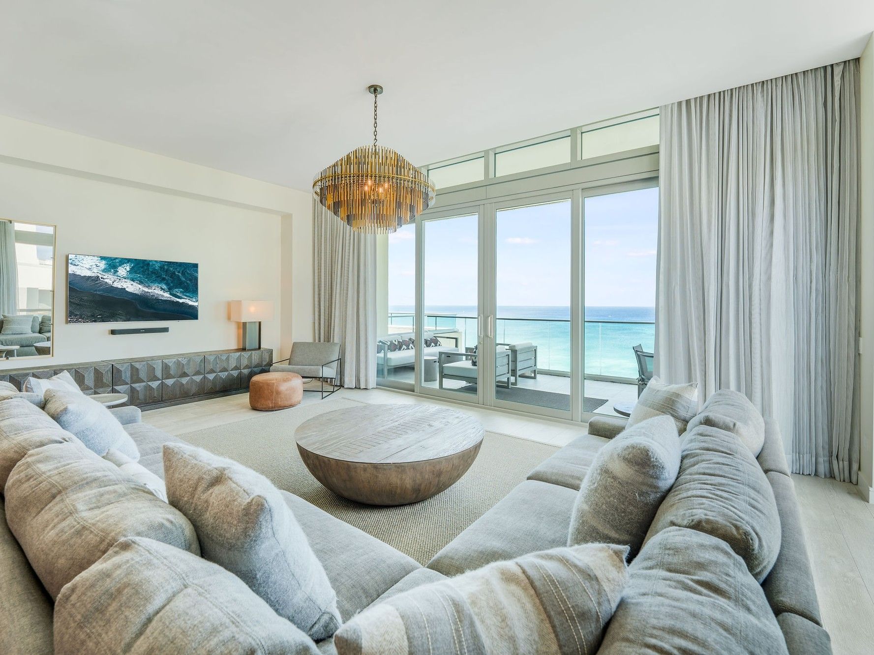 Living room with large couch, glass doors, ocean view, and modern decor at the N1002 Room at the Seafire Residences.