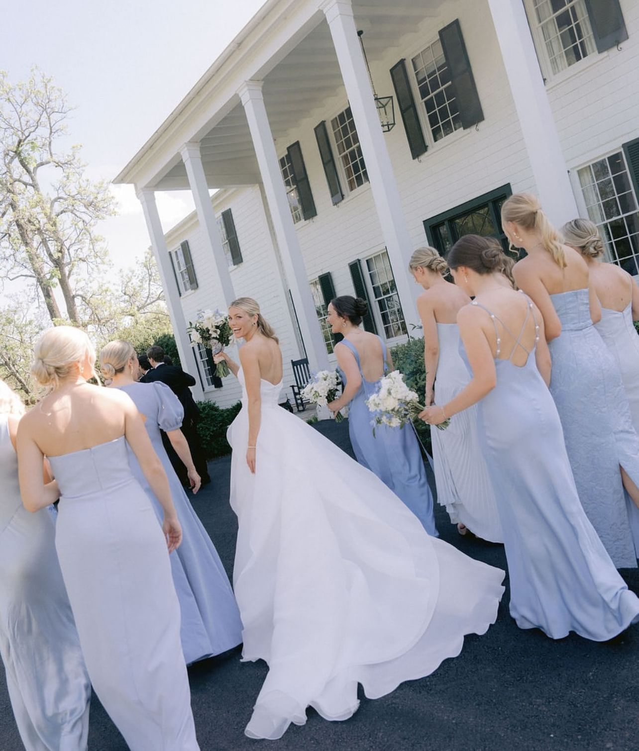 Bride and bridesmaids in blue dresses and white gown, standing outside The Clifton Hotel in Charlottesville, VA.