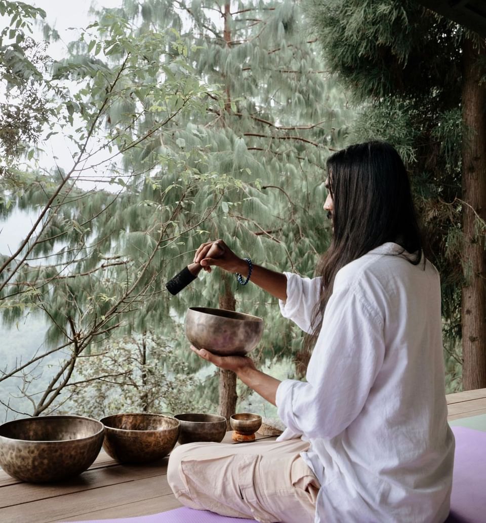 Person with singing bowls on a porch overlooking a forest at The Terraces Resort & Spa