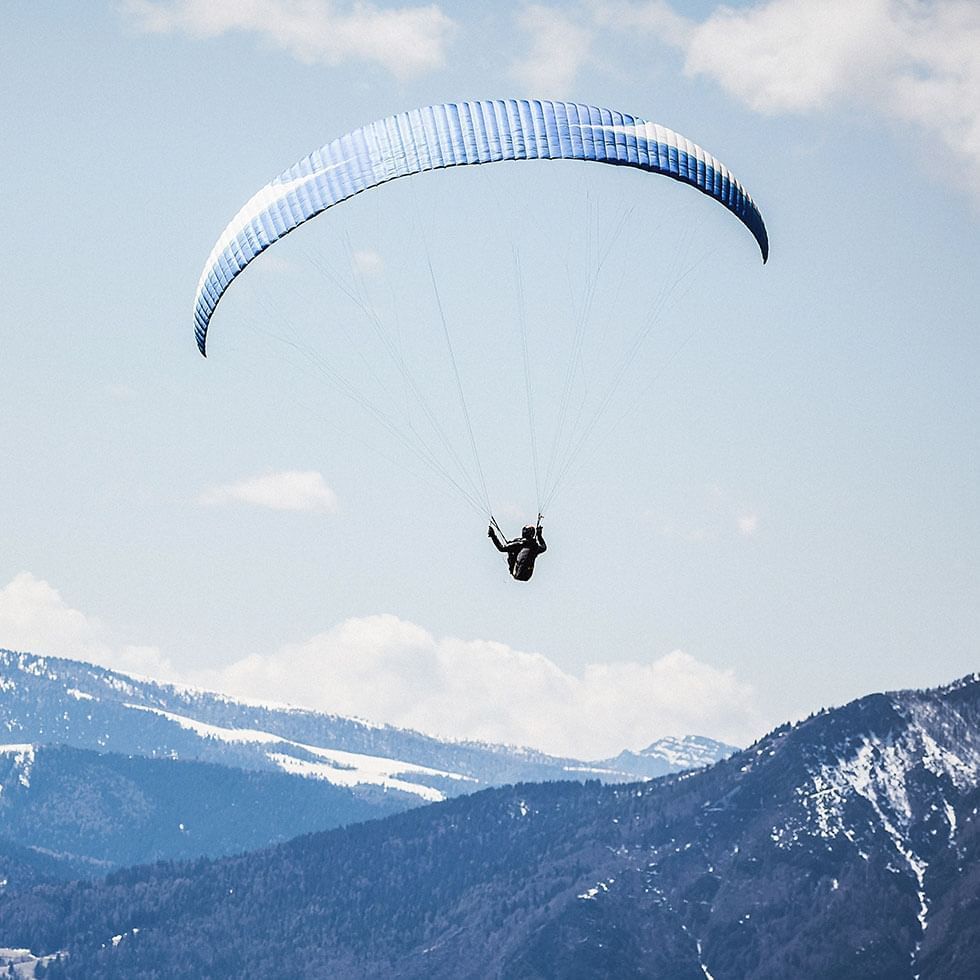 Person paragliding with a wing over snowy mountains near Falkensteiner Hotel Kronplatz