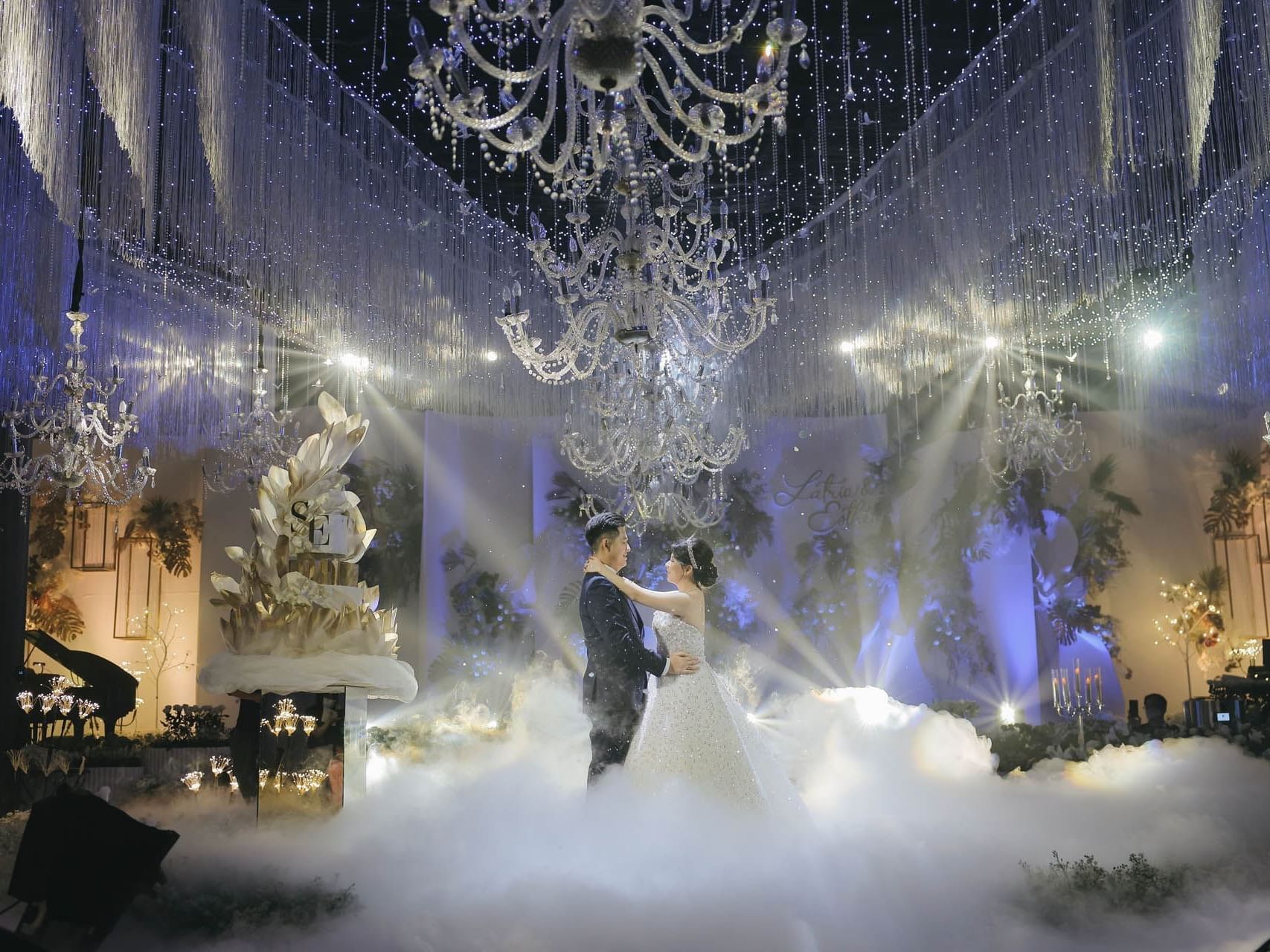 A couple dances amidst a wedding venue adorned with chandeliers, soft fog, and sparkling lights at Vasa Hotel Surabaya