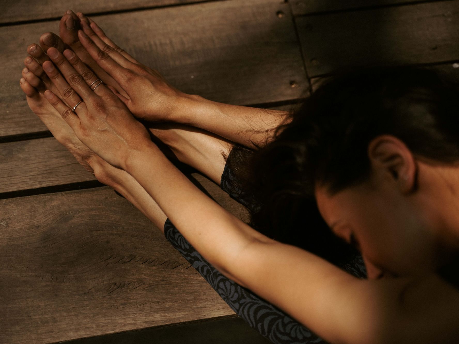 Close-up of two hands reaching toward flexed feet on a wooden surface at Dwarika's Himalayan Wellbeing