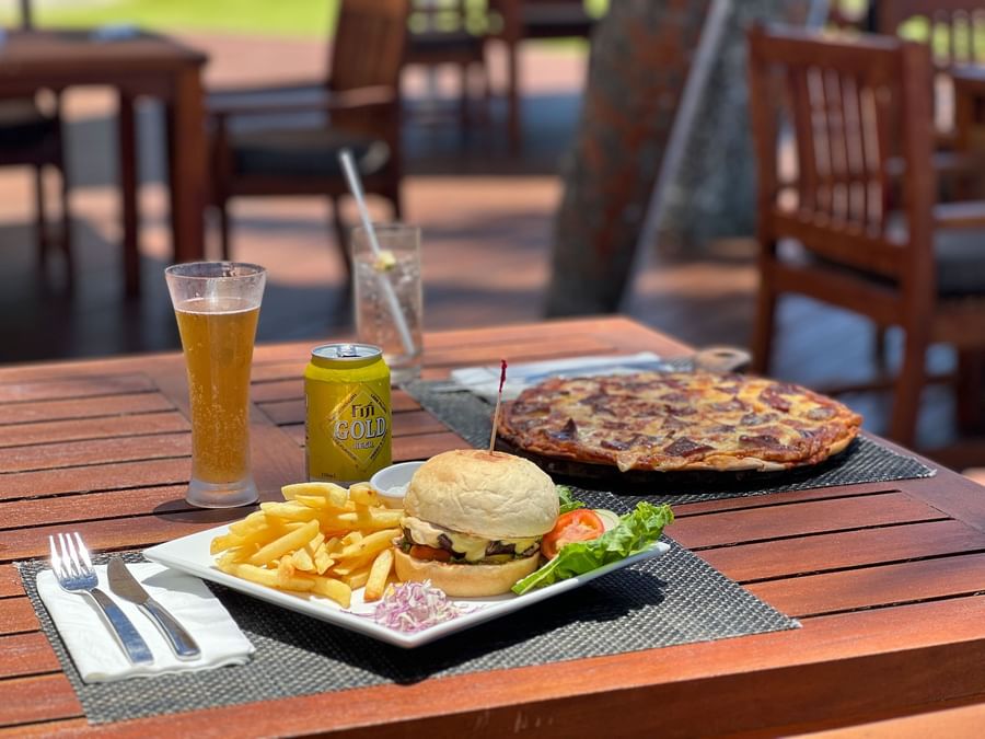 Plate with burger, fries, and pizza on wooden table at Warwick Fiji Resort and Spa.