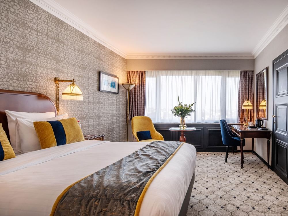 Elegante familiekamer met een groot bed, een stoel, een bureau en een raam met uitzicht op de stad in Hotel Barsey by Warwick – Brussel.