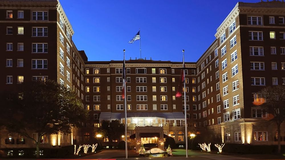 Exterior view of the entrance by lit trees under a twilight sky at Warwick Melrose Dallas