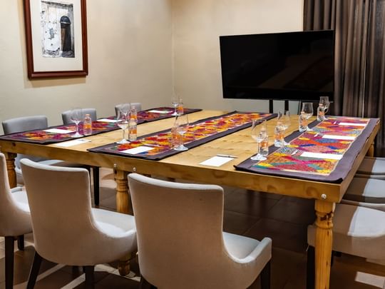 Long wooden table with place settings and a TV at Quinta Real Puebla in Heroica Puebla de Zaragoza.