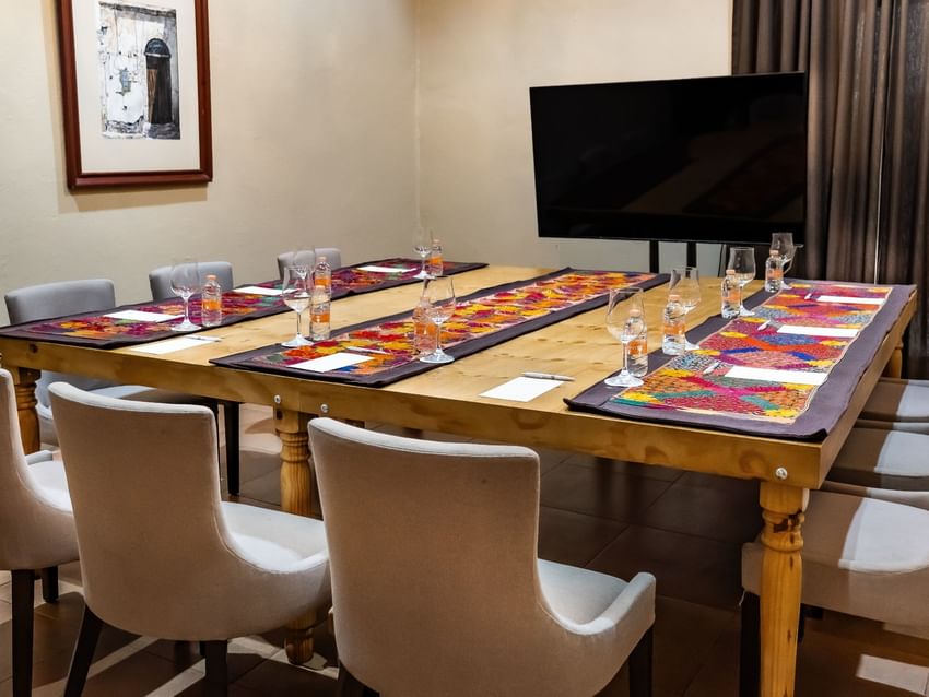 Long wooden table with place settings and a TV at Quinta Real Puebla in Heroica Puebla de Zaragoza.
