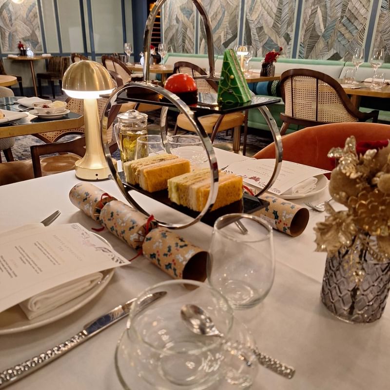 A dining table set with silverware, glasses, a vase, and a tiered tray of desserts.
