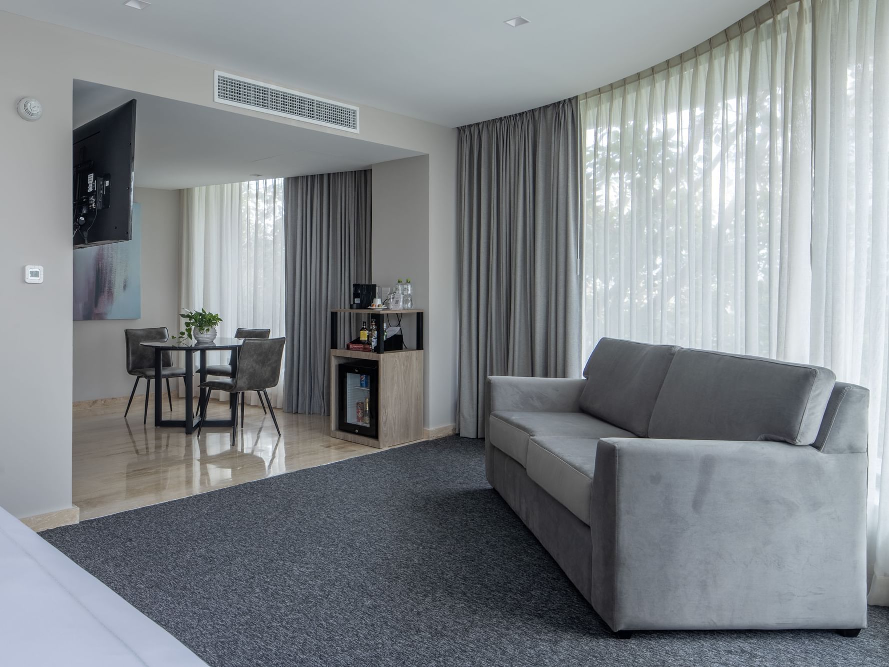 Living area with gray couch, carpet, and dining table in Elements Suite at Elements by Marquis in Ciudad de México.