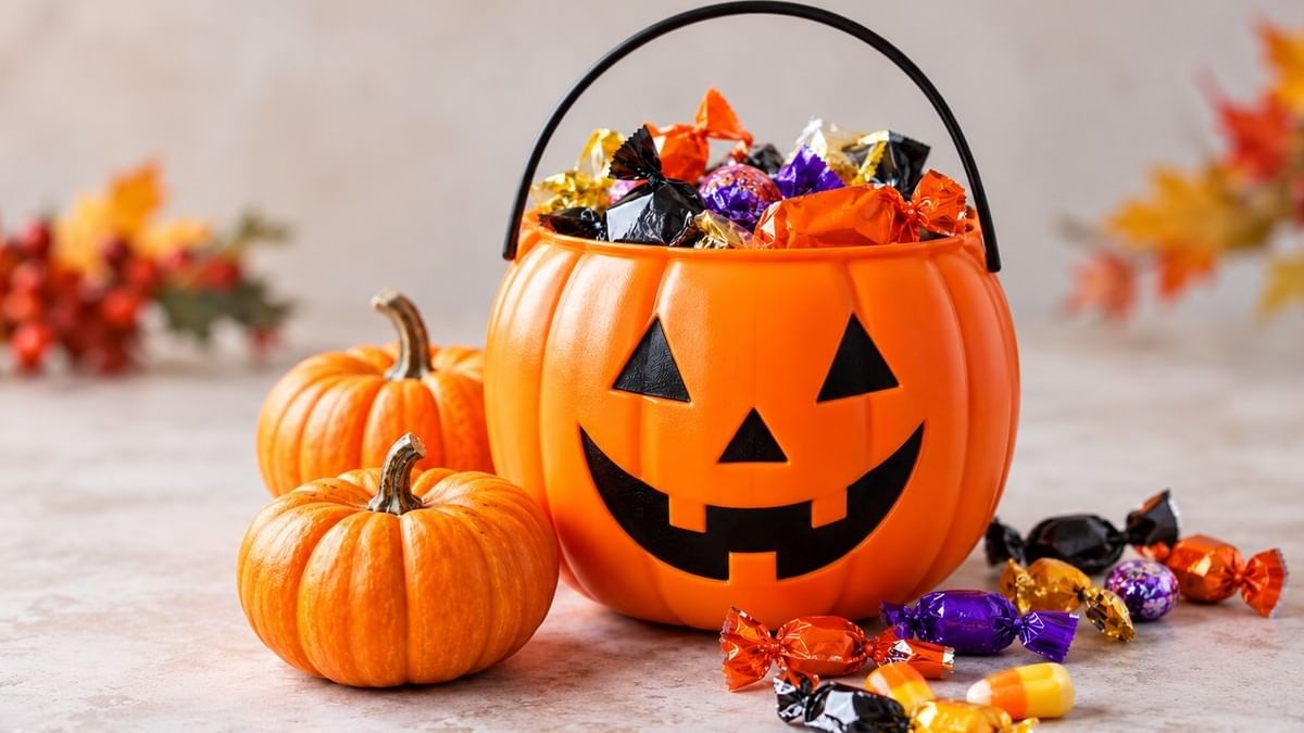 Orange jack-o'-lantern bucket filled with wrapped candies surrounded by small pumpkins and autumn decorations.