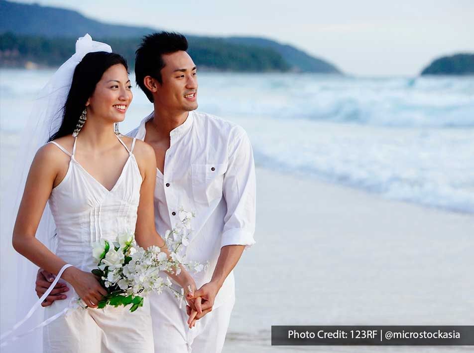 A woman wearing a wedding dress was walking on the beach with her husband - Lexis Suites Penang