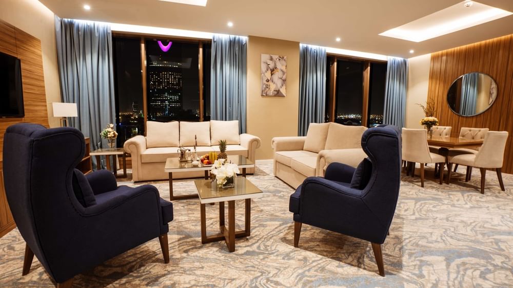 Elegant living area with sofas by a dining set under blue drapes at night in Royal Suite at Cantonal Hotel by Warwick Riyadh