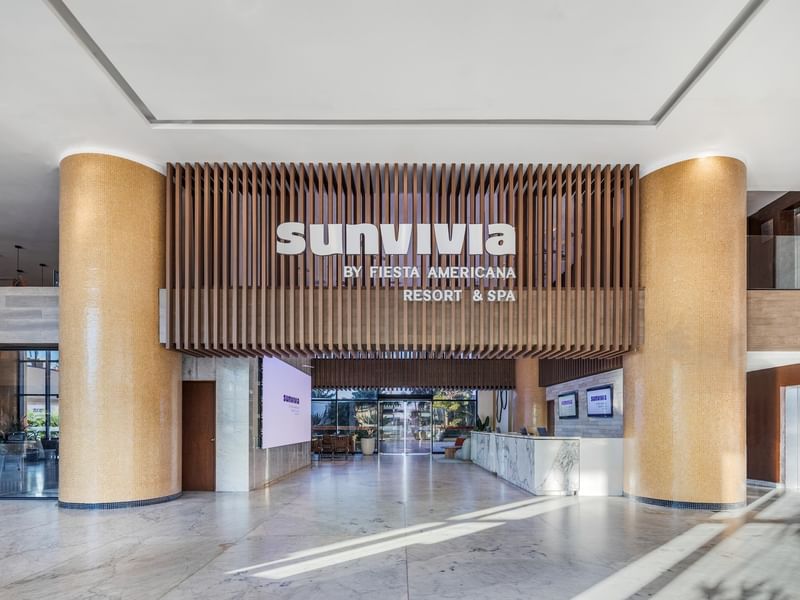 Sunvivia Mazatlán resort lobby with marble floors, gold columns, and a large Sunvivia Resort & Spa sign on wooden slats