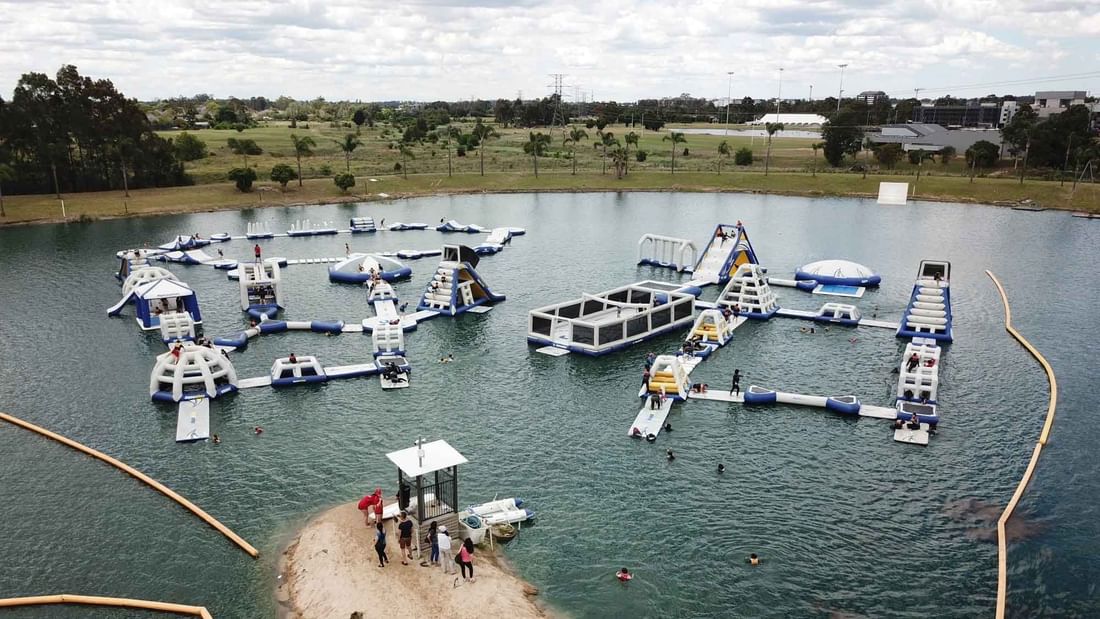 Aerial view of a water park with inflatable obstacles and slides floating on a lake.