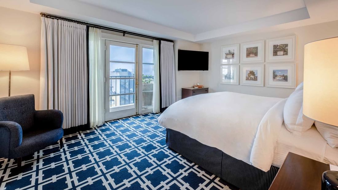 Penthouse with cozy bed, patterned carpet, and French doors leading to a balcony at El Prado Hotel