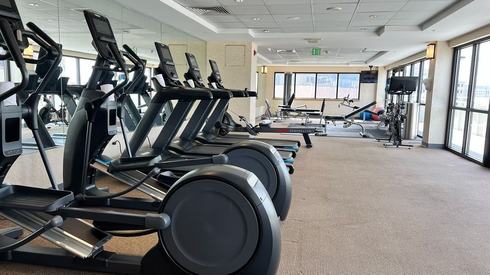 Row of treadmills by a mirror under a tiled ceiling near gym equipment at Warwick Denver