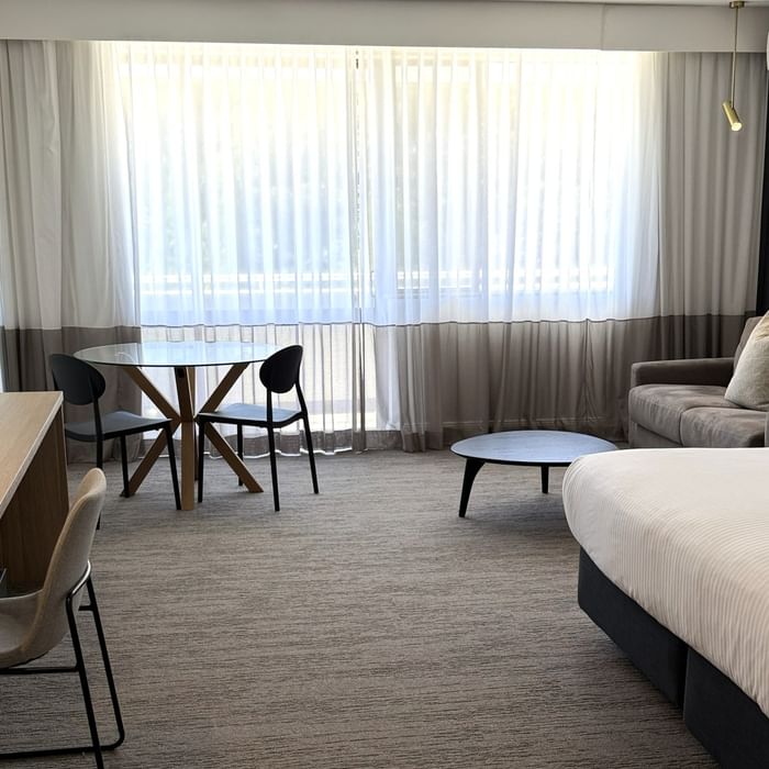 Elegant room with a large bed, desk, couch, and table at Mercure Charlestown.