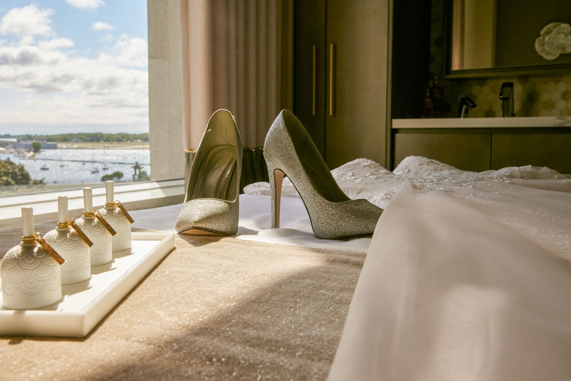 Silver high heels and bridal gown on bed facing window with waterfront view in wedding suite at Hotel X Toronto