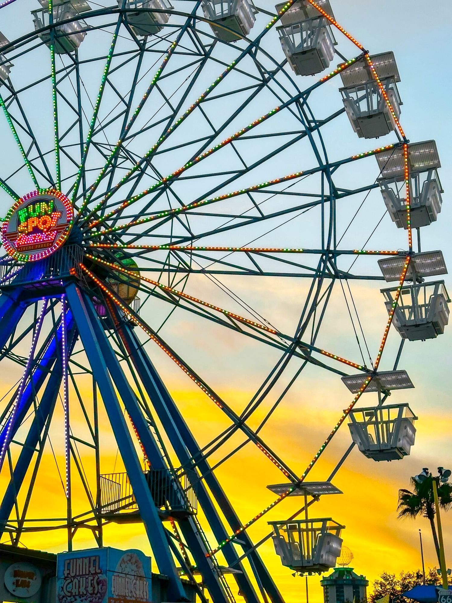 A close-up of a Ferris wheel with the Fun Spot logo in the middle silhouetted against a sunset sky.