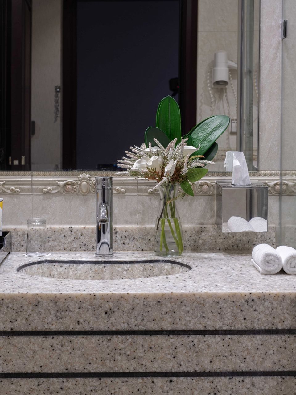 Granite sink with flower vase by a mirror and toiletries a bathroom in Standard Room at Warwick Al Jubail