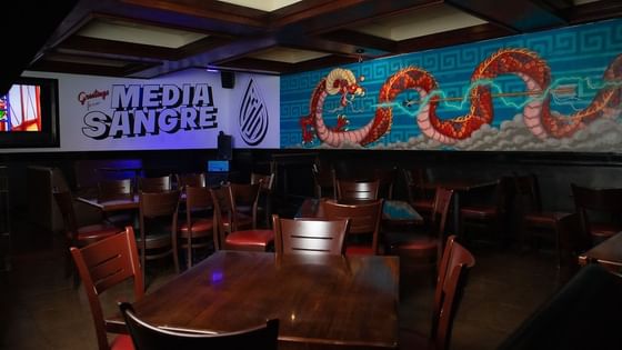 Spacious dining area featuring wooden seating and vibrant dragon wall mural inside Media Sangre at Araiza Calafia