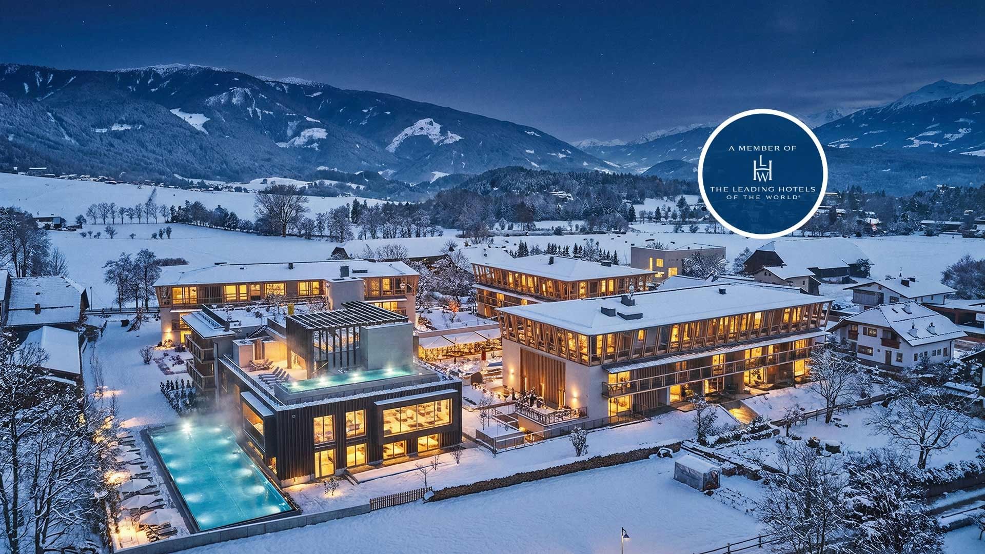 A snowy mountain resort with lit buildings and pool at Falkensteiner Hotel Kronplatz