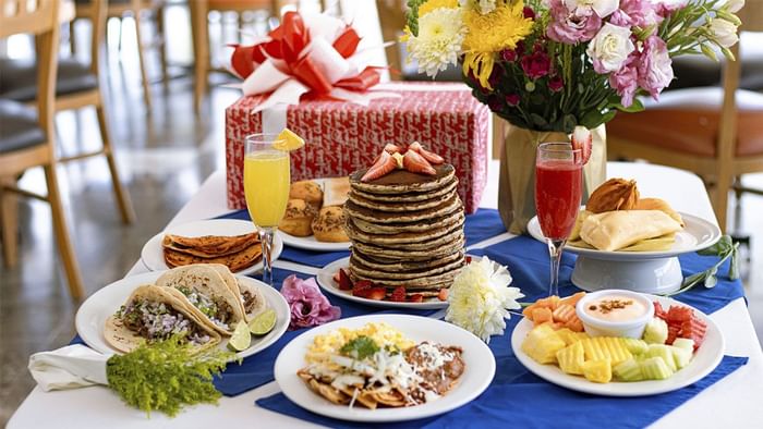 Desayuno festivo con pila de panqueques, tacos y fruta sobre camino azul en La Pérgola de Araiza Palmira 
