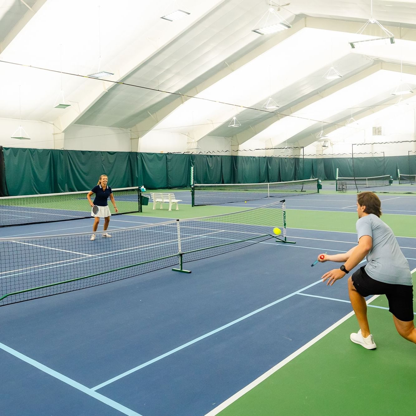 Three pairs of people playing pickleball on an indoor court at a Beginner's Pickleball Clinic.
