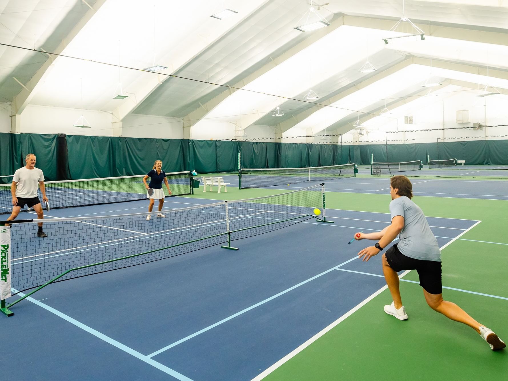 Three pairs of people playing pickleball on an indoor court at a Beginner's Pickleball Clinic.