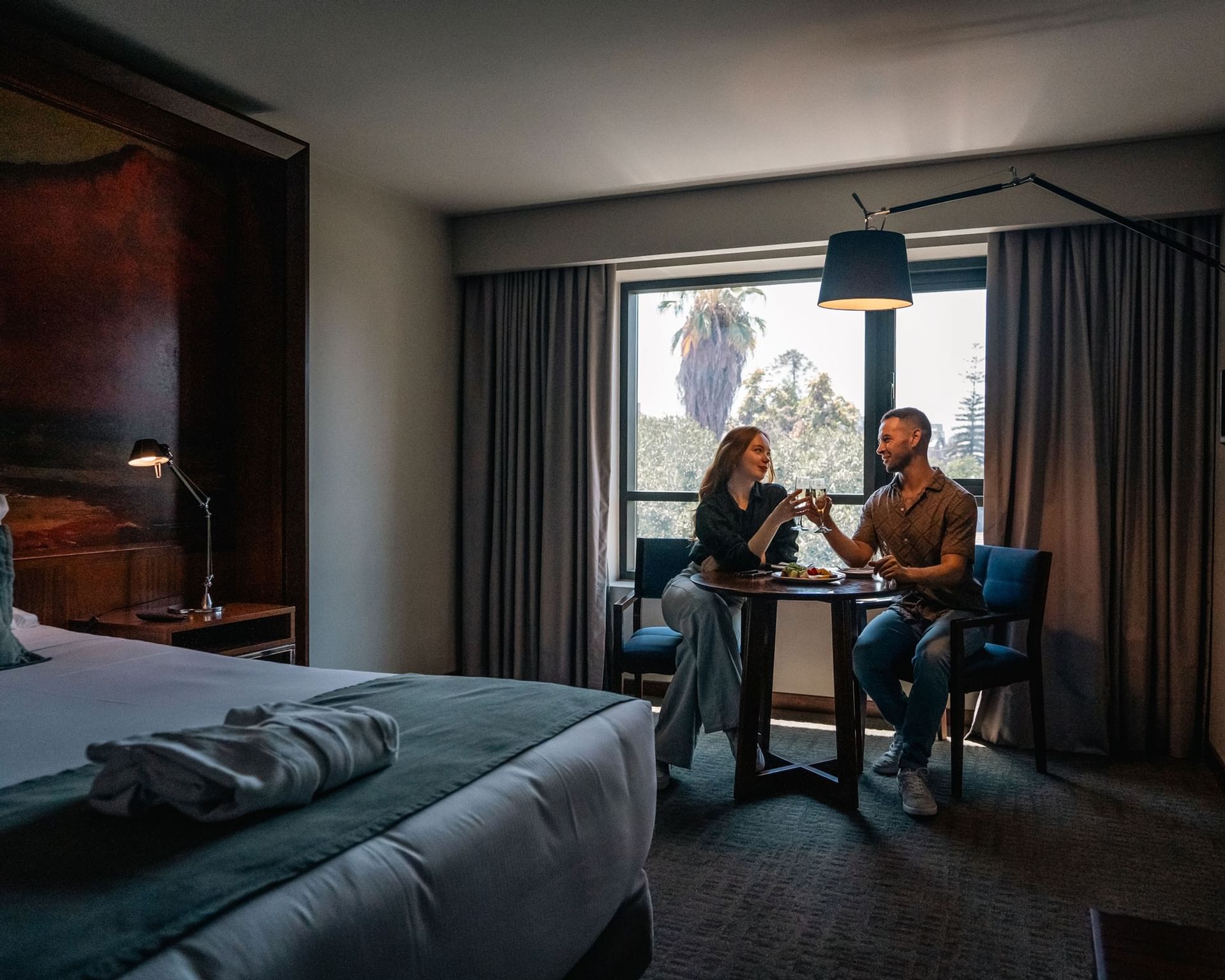 Pareja brindando con vino en habitación moderna con vista a palmeras en Cumbres Lastarria