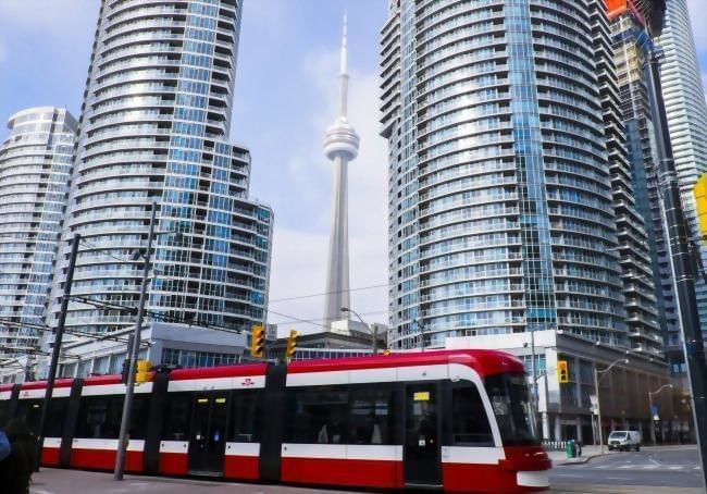 Toronto Transit Commission moving on street with tall skyscrapers facing CN Tower in downtown district near Hotel X Toronto