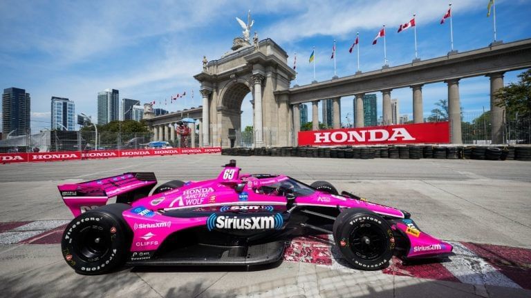 Pink race car on street course beside historic arch and Honda signage during Honda Indy event near Hotel X Toronto
