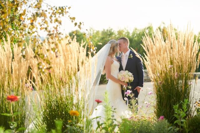 Newlyweds kissing on bridge surrounded by lush green foliage and wild flowers at Mountain View Grand Resort & Spa
