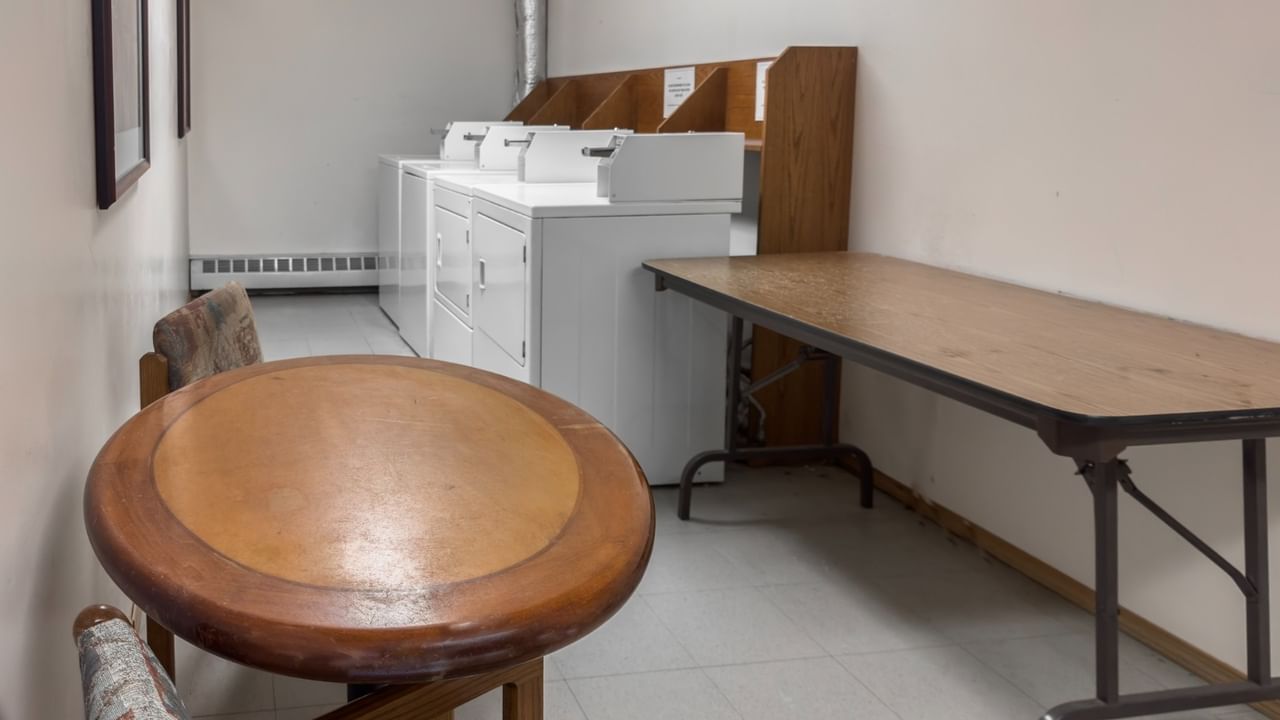 A laundry room with a table, a chair, and washing machines.